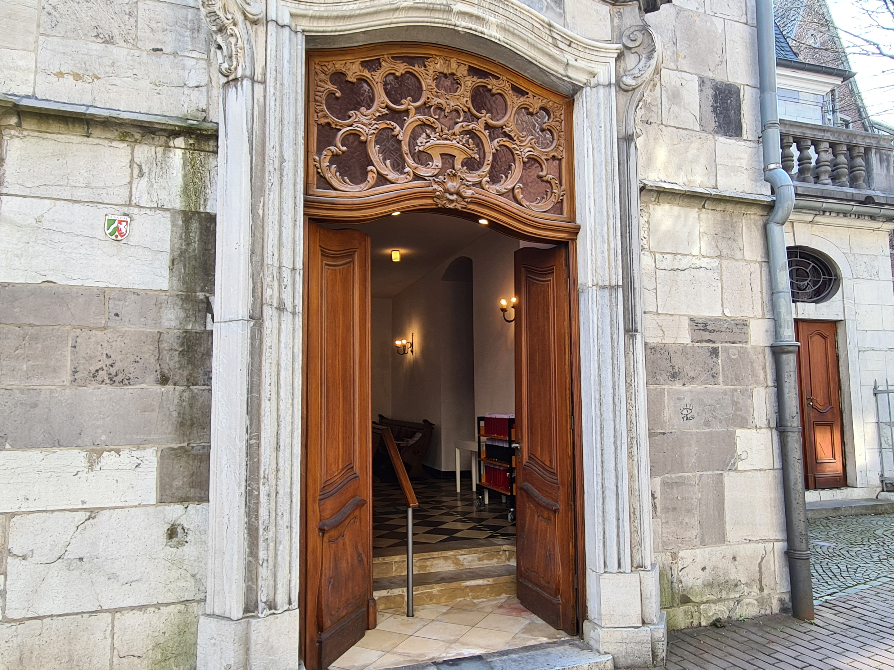 Eine offene Holztür einer alten Kirche mit barocken Verzierungen.