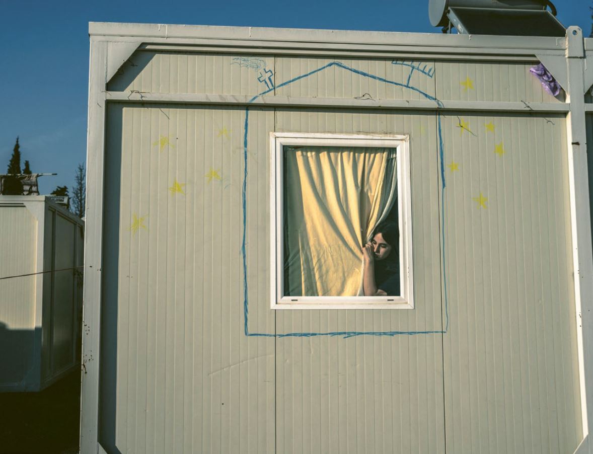 Ansicht eines Wohncontainers im Flüchtlingslager. Hinter dem Vorhang am Fenster ist eine Frau zu sehen.